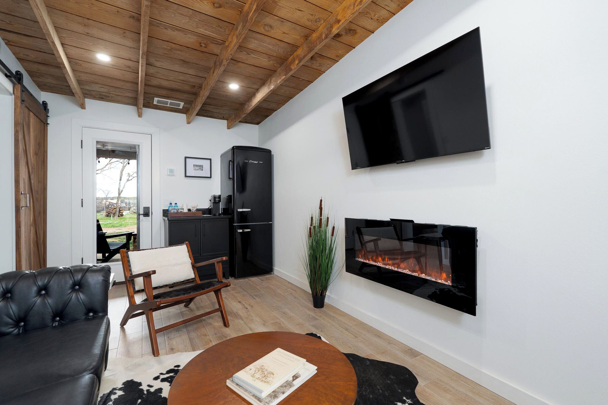 Sala de estar com lareira, televisão de tela plana, sofá preto e área de jantar com mesa e cadeiras.