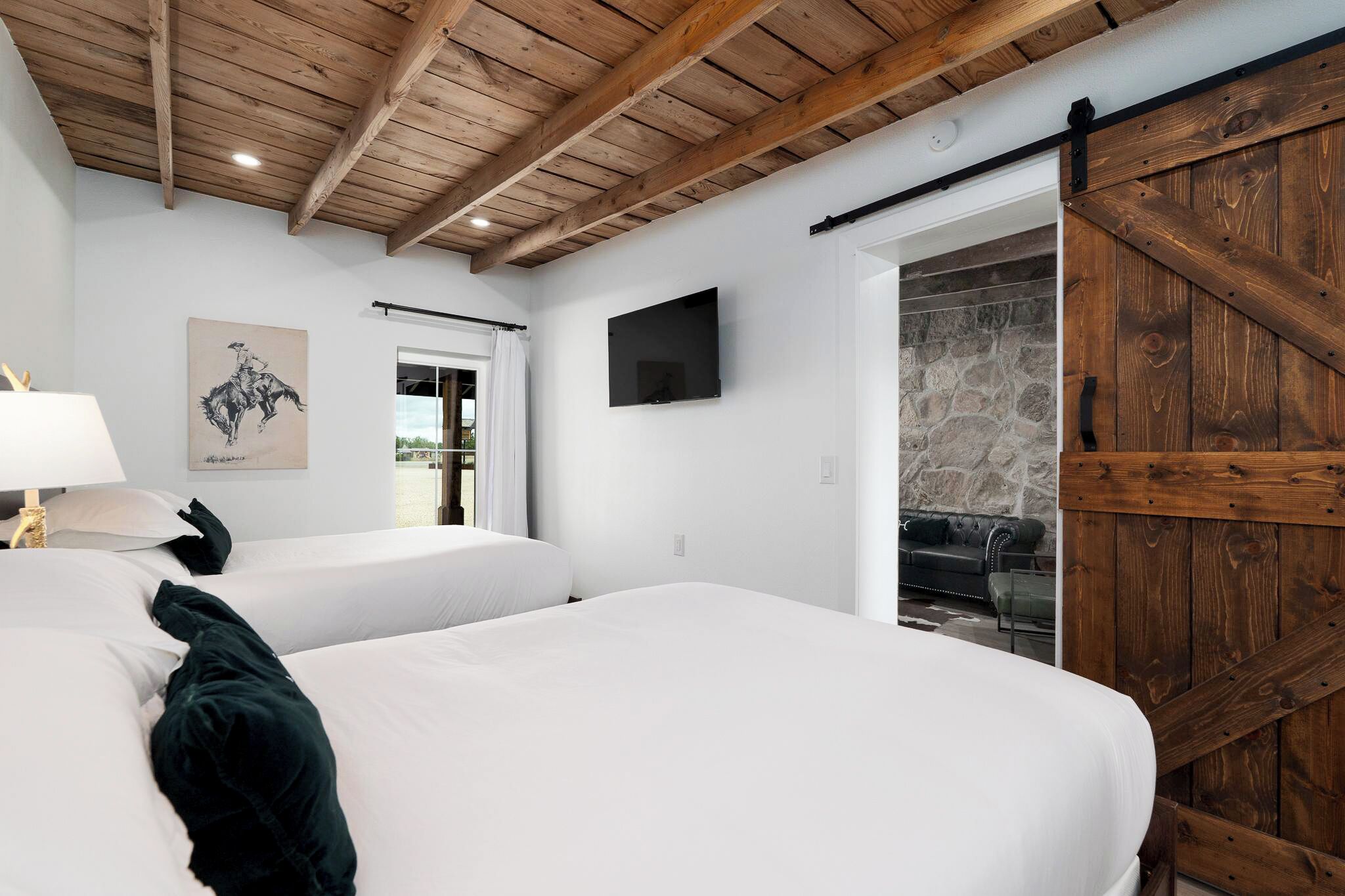 A hotel room with two beds, a wooden ceiling, a stone wall, and a sliding barn door.