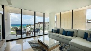 A modern living room with a large glass window, a sofa, and a coffee table. - Ocd35- Luxury Condo With Ocean View (Playa del Carmen)