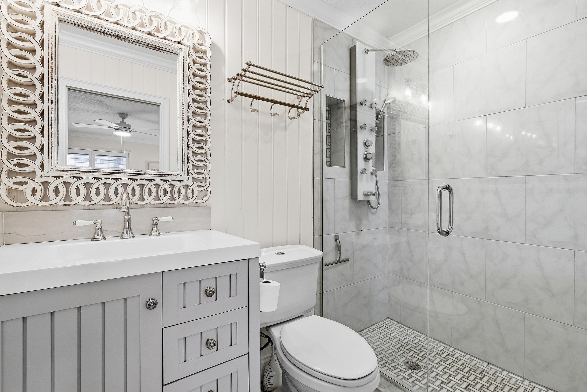 A bathroom with a vanity, sink, mirror, toilet, and shower.