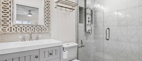 A bathroom with a vanity, sink, mirror, toilet, and shower.