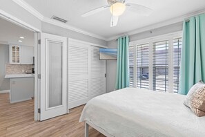 Une chambre à coucher avec un lit, un ventilateur de plafond, une télévision et une vue sur l’extérieur grâce à de grandes fenêtres.