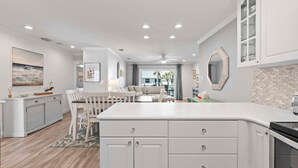A modern kitchen with white cabinetry, a central island, and a dining area with a sofa and chairs. - Colony Beach Club 248 (New Smyrna Beach)