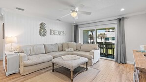 A living room with a sectional sofa, a coffee table, a side table with a lamp, and a ceiling fan. - Colony Beach Club 248 (New Smyrna Beach)