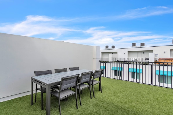 A rooftop terrace with a table and chairs, surrounded by a white wall and a metal fence.