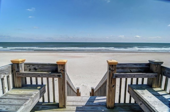 A wooden boardwalk leading to a beach with a clear view of the ocean.