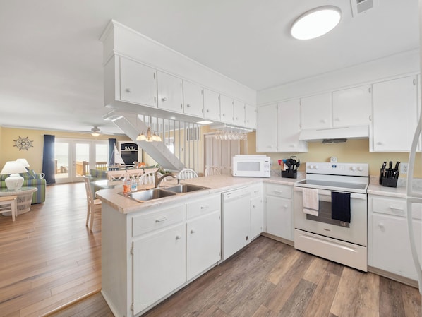 A modern kitchen with white cabinetry, a built-in microwave, and a stainless steel sink. - All About The View by Topsail Realty (Holly Ridge)