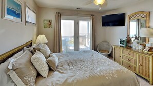 Quarto de hotel com uma cama grande, televisão, penteadeira e varanda com vista.