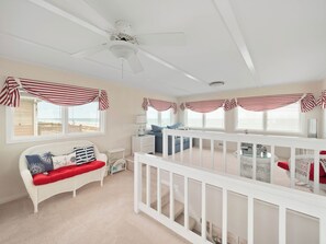 A beachside room with a white ceiling fan, a white wicker sofa with red cushions, a blue sofa, and a white railing. - All About The View by Topsail Realty (Holly Ridge)