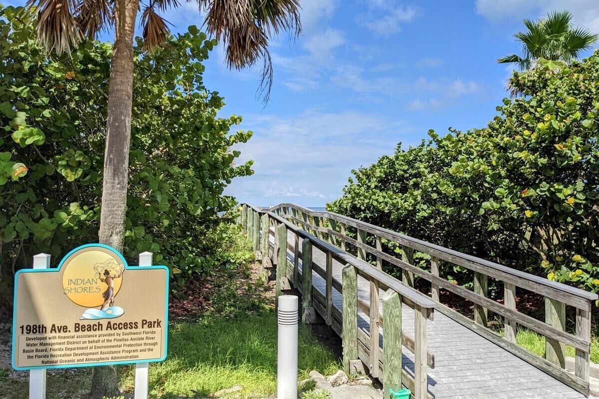 Un puente de madera que conduce a un parque de acceso a la playa, con un cartel que indica que es el Parque de Acceso a la Playa de la Avenida 198.