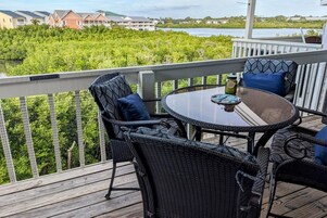 Una terrazza con mobili in vimini e un tavolo in vetro, con vista su un corpo d'acqua e vegetazione.