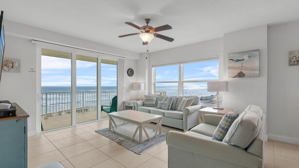 A spacious living room with a large window overlooking the sea, a ceiling fan, and a cozy seating area. - Aruba 206 (Daytona Beach Shores)
