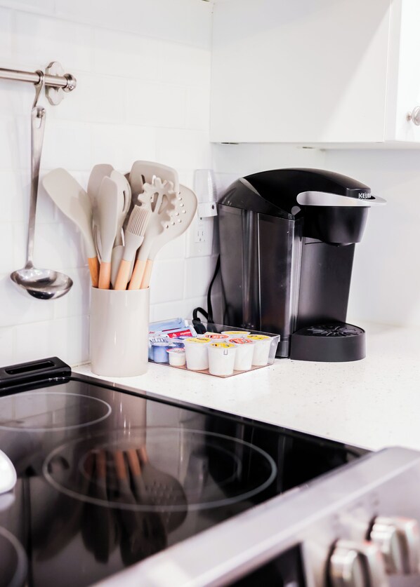 A kitchen with a black Keurig coffee maker, a white container with utensils, and a stove.