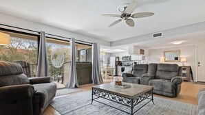 Un salón amplio con ventilador de techo, una zona de comedor con mesa y sillas, y una cocina al fondo.