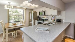 Una cocina moderna con armarios blancos, encimera de granito y un comedor con mesa y sillas de madera.