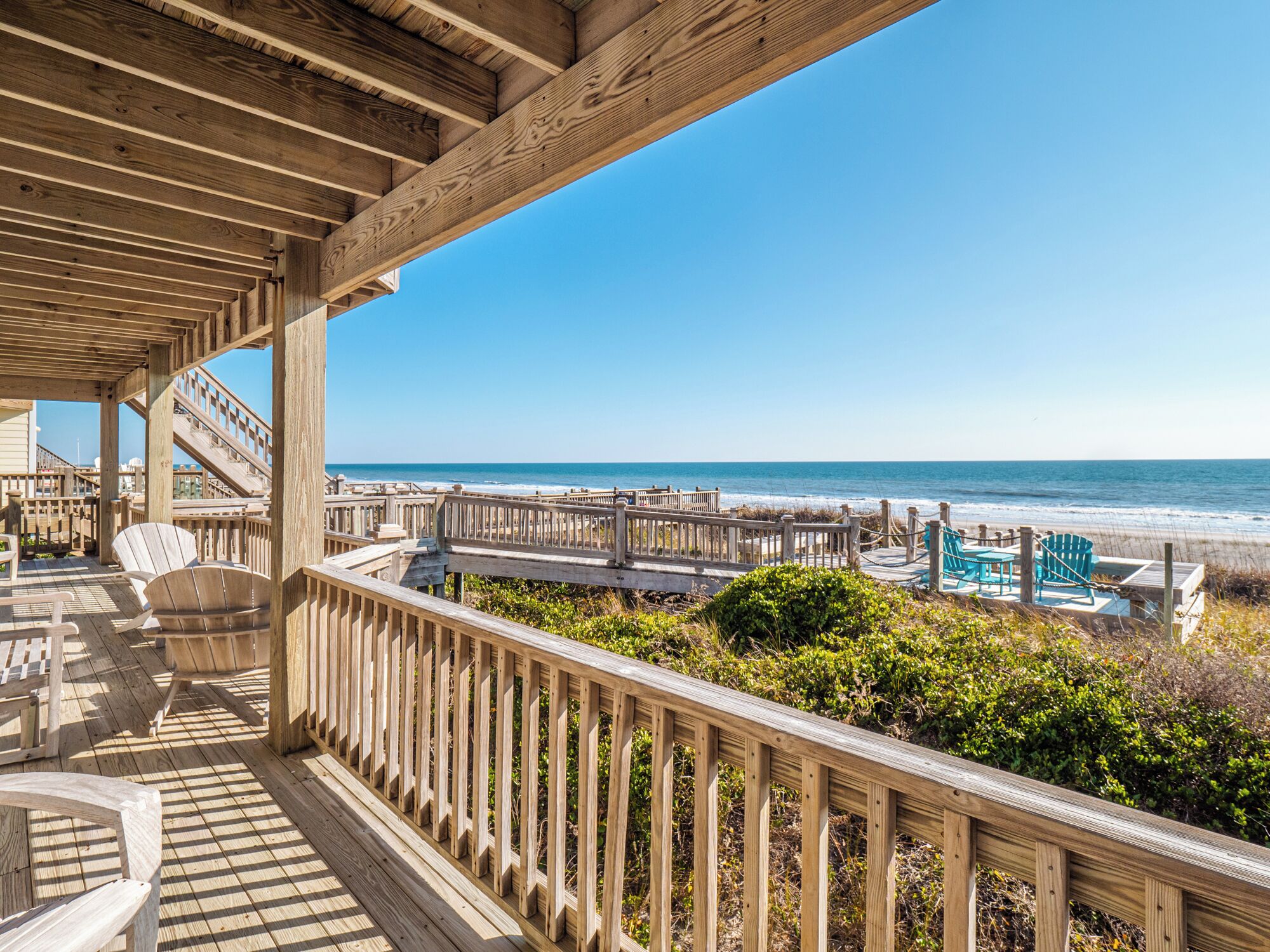 Eine Holzterrasse mit Stühlen und Poolbereich mit Blick auf den Strand.