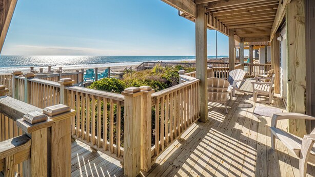 Una terraza de madera con vista a la playa y al océano.