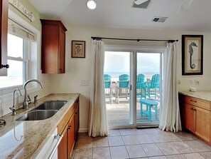A kitchen with a view of the beach, a sliding glass door, and a dining area with chairs. - Carrle/Trachtman by Topsail Realty (Holly Ridge)