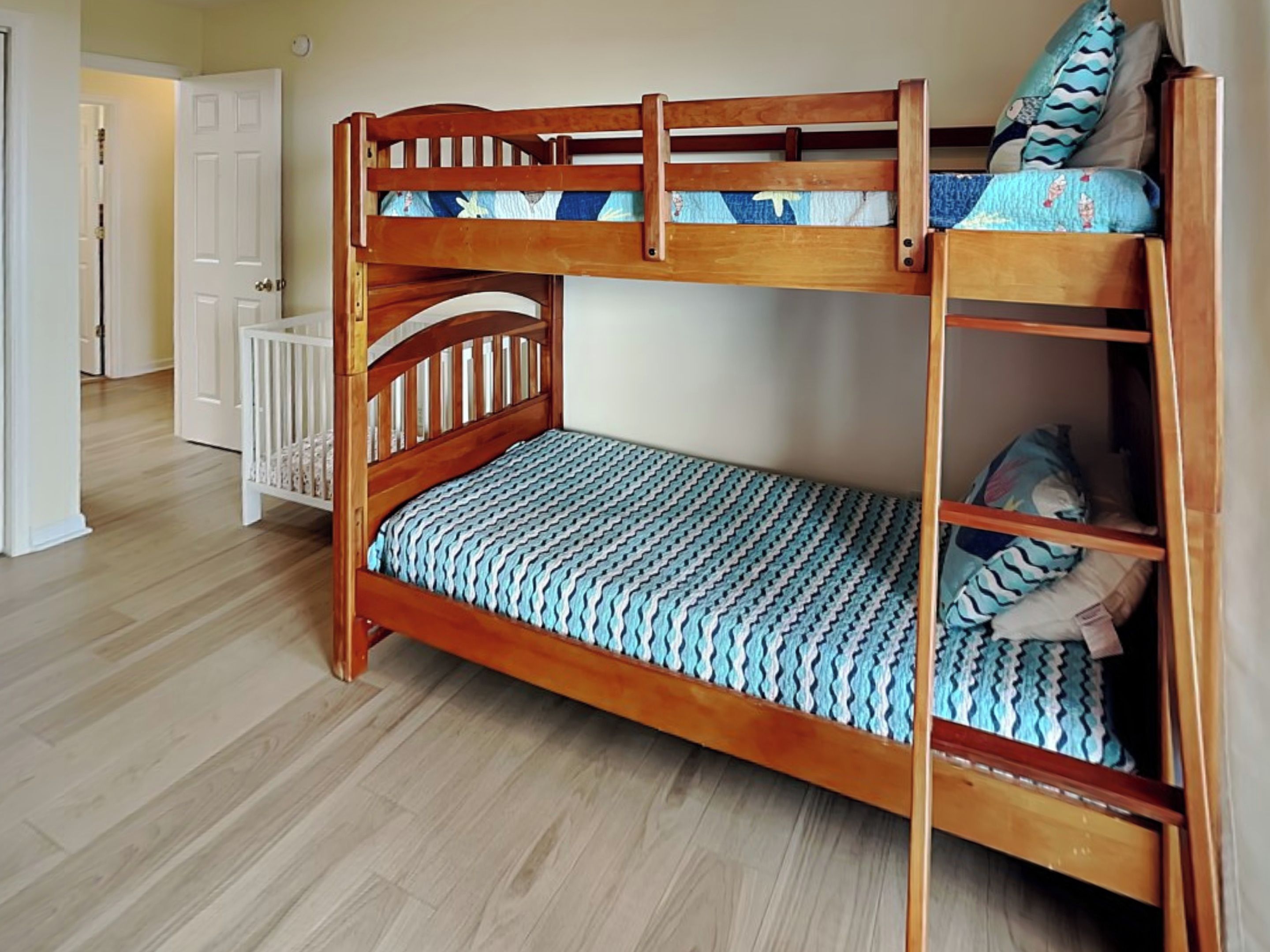 Una cama individual doble con estructura de madera, la cama inferior con un colchón estampado y la superior con almohadas y una colcha.
