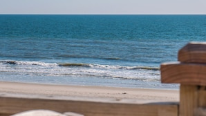 Una playa con una valla de madera en primer plano y una vista despejada del océano.