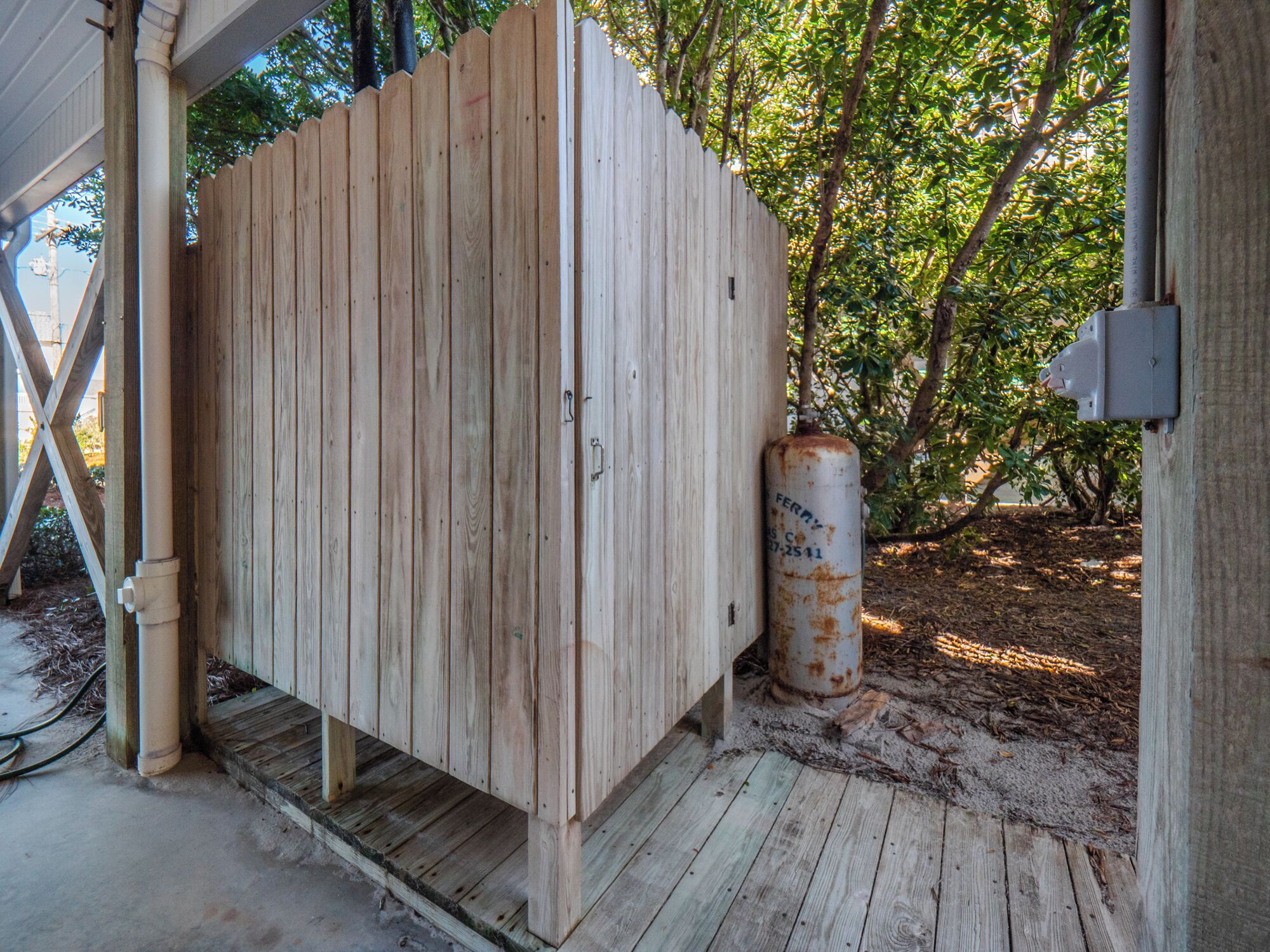 A wooden shed with a metal cylinder attached to it, situated under a covered area with a concrete floor.
