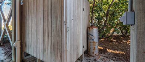 A wooden shed with a metal cylinder attached to it, situated under a covered area with a concrete floor.