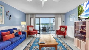 Un salon avec un canapé bleu, deux fauteuils rouges, une table basse en bois et un grand téléviseur.