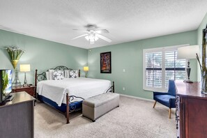 Une chambre à coucher avec un lit, un bureau, une chaise, une fenêtre et un ventilateur de plafond.