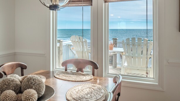 Un área de comedor con vista al océano, que incluye una mesa de madera, sillas y una lámpara colgante.
