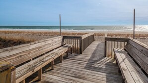 Un paseo marítimo de madera que conduce a una playa con bancos.