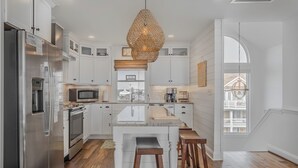 Una cocina moderna con armarios blancos, electrodomésticos de acero inoxidable y una isla central con taburetes.
