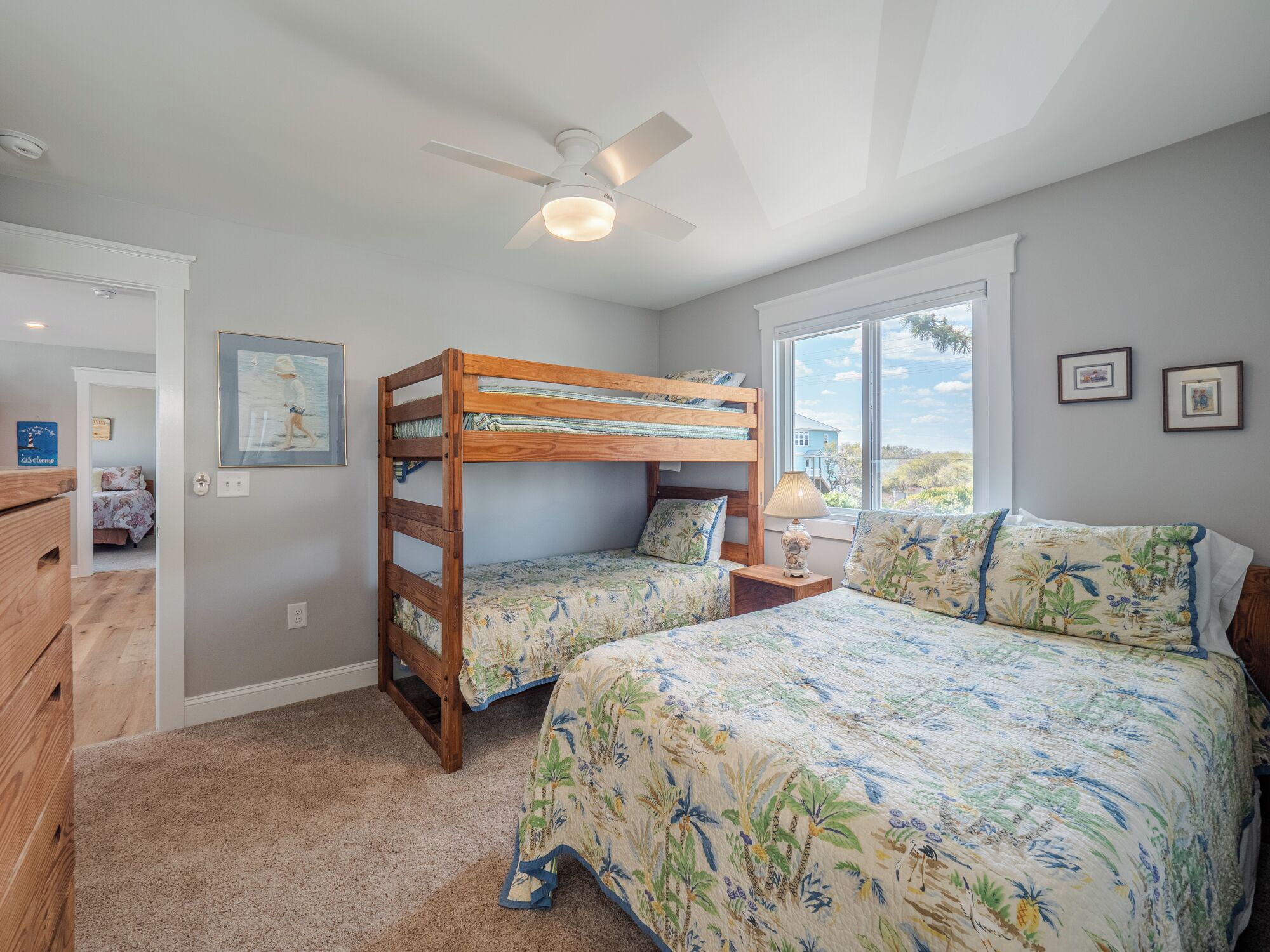 A bedroom with bunk beds, a ceiling fan, a window with a view, and a door leading to another room.