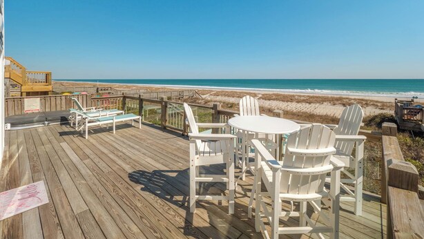 A wooden deck with white chairs and a table overlooking a beach. - Beach Coma by Topsail Realty (Holly Ridge)