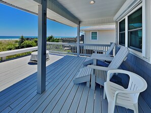 A covered porch with a view of the beach, white plastic chairs, and a small table. - A Beach Pearle by Topsail Realty (Holly Ridge)