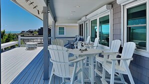 Una terraza techada al aire libre con sillas Adirondack blancas y una mesa, con vistas a un paisaje pintoresco.
