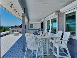 A covered outdoor deck with white Adirondack chairs and a table, overlooking a scenic view.