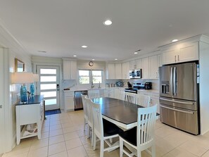 A modern kitchen with white cabinetry, a central island with seating, stainless steel appliances, and a clock on the wall.