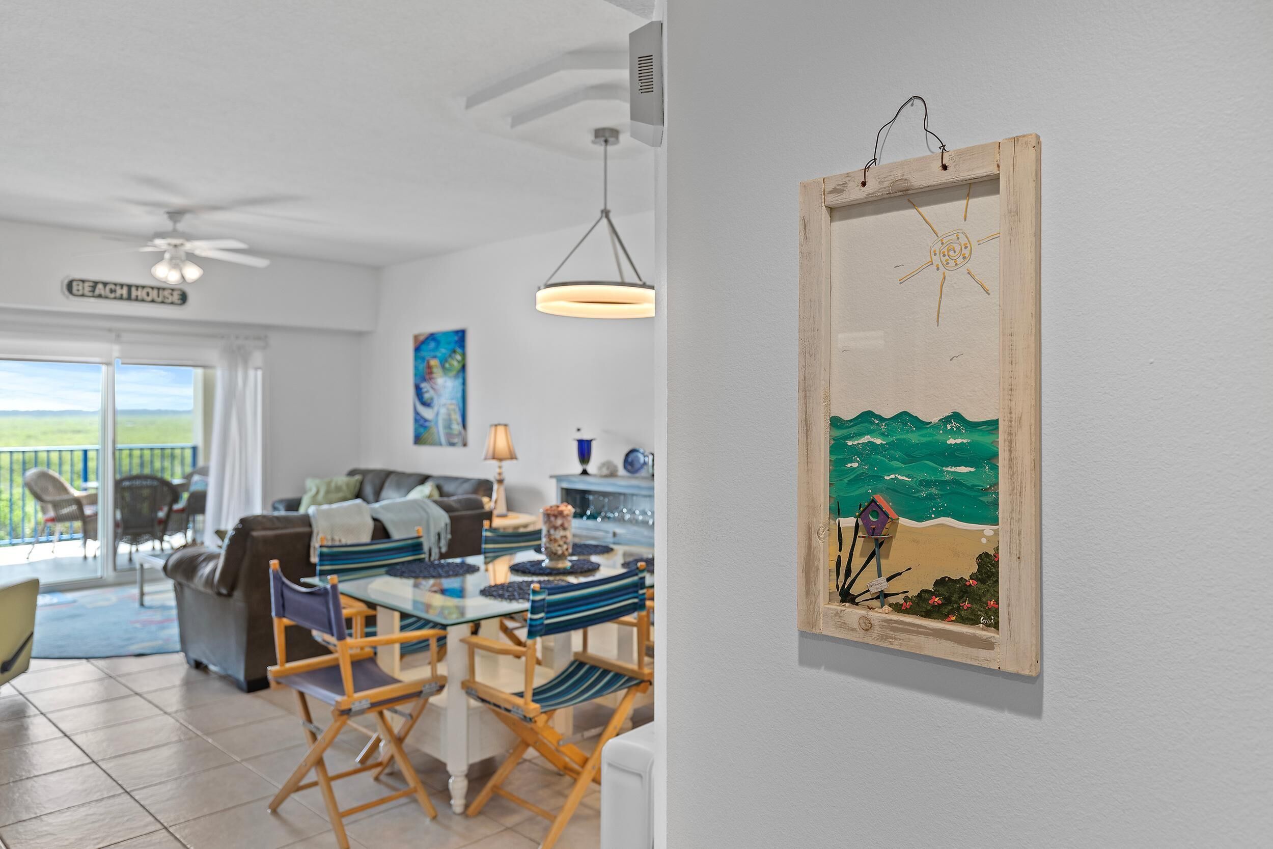 Een eethoek met een tafel en stoelen, een plafondventilator en een schilderij van een strand.