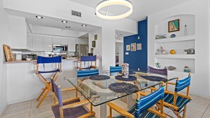 Une cuisine moderne avec des meubles blancs, un four à micro-ondes et un coin repas comprenant une table en verre et des chaises à rayures.