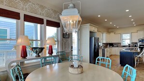 A kitchen with a round table, teal chairs, and a hanging light fixture. - Oceans 111 by Topsail Realty (Holly Ridge)
