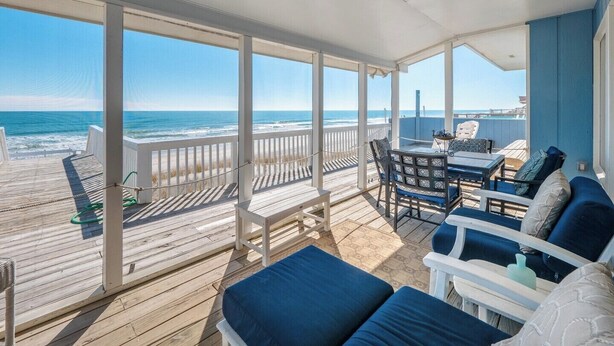 A covered outdoor deck with a view of the ocean, furnished with blue and white chairs and a table. - The Shark and the Seahorse by Topsail Realty (Holly Ridge)