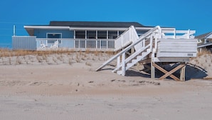A beach house with a blue exterior, white railings, and a wooden staircase leading to a deck. - The Shark and the Seahorse by Topsail Realty (Holly Ridge)