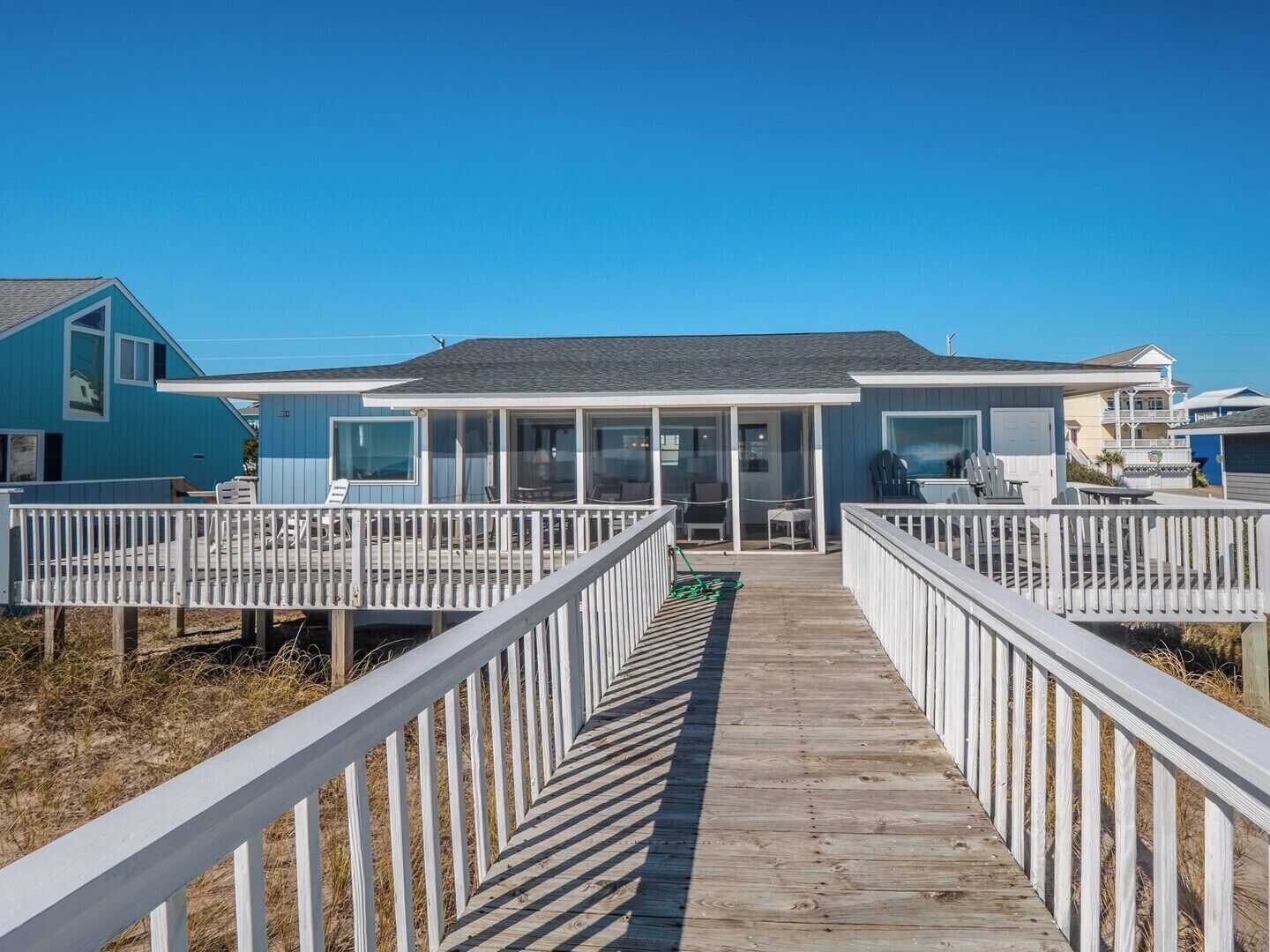 A beachfront property with a wooden deck leading to a covered patio area with outdoor seating.