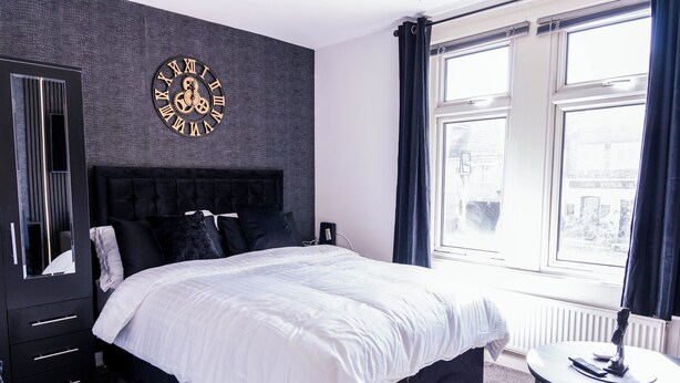 A modern bedroom with a large bed, a wall clock, a dresser, and a window with curtains. - Charming Dartford Apartment - Ideal for Explorers! (Dartford)