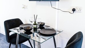 A modern dining area with a glass table, two black chairs, and a flat-screen TV mounted on the wall. - Charming Dartford Apartment - Ideal for Explorers! (Dartford)