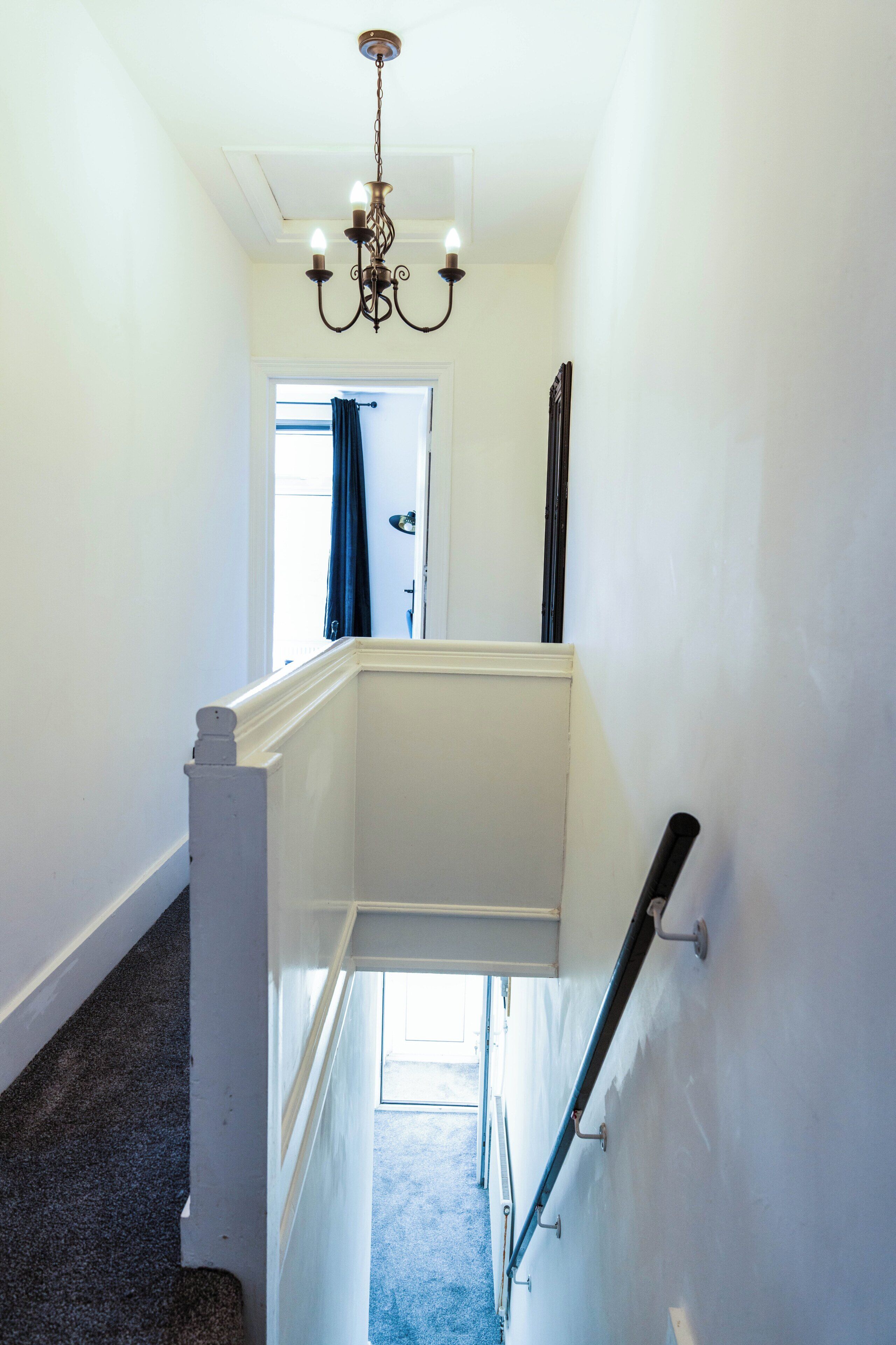 A staircase with a white handrail and a black banister, leading to a landing with a chandelier.