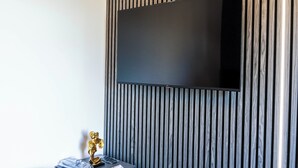 A modern room with a large flat-screen TV mounted on a wooden panel wall. - Charming Dartford Apartment - Ideal for Explorers! (Dartford)