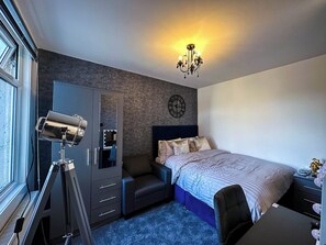 Une chambre à coucher moderne avec un grand lit, une coiffeuse avec un miroir et des lampes, un bureau et un lustre.