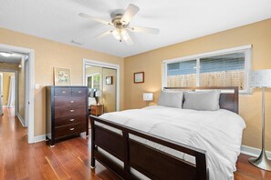 A bedroom with a wooden bed, a ceiling fan, a dresser, and a window with blinds. - Evergreen (New Smyrna Beach)