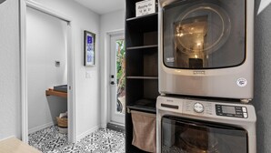 A laundry area with stacked appliances, a door leading to a room, and patterned flooring. - Evergreen (New Smyrna Beach)